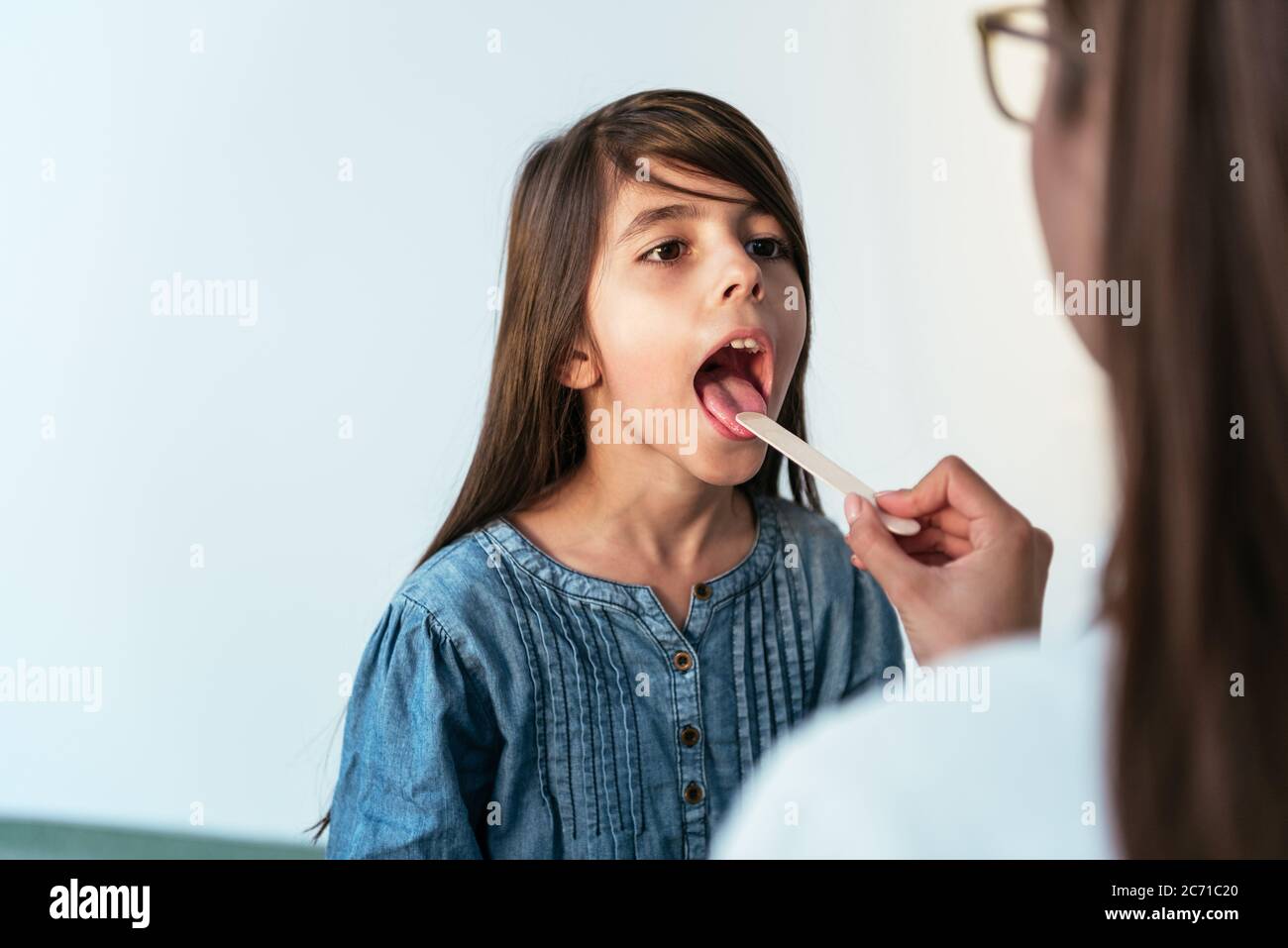 Femme médecin examinant une petite fille à l'hôpital vérifiant le mal de gorge. Le pédiatre vérifie les amygdales d'un petit patient dans la chambre d'hôpital. Banque D'Images