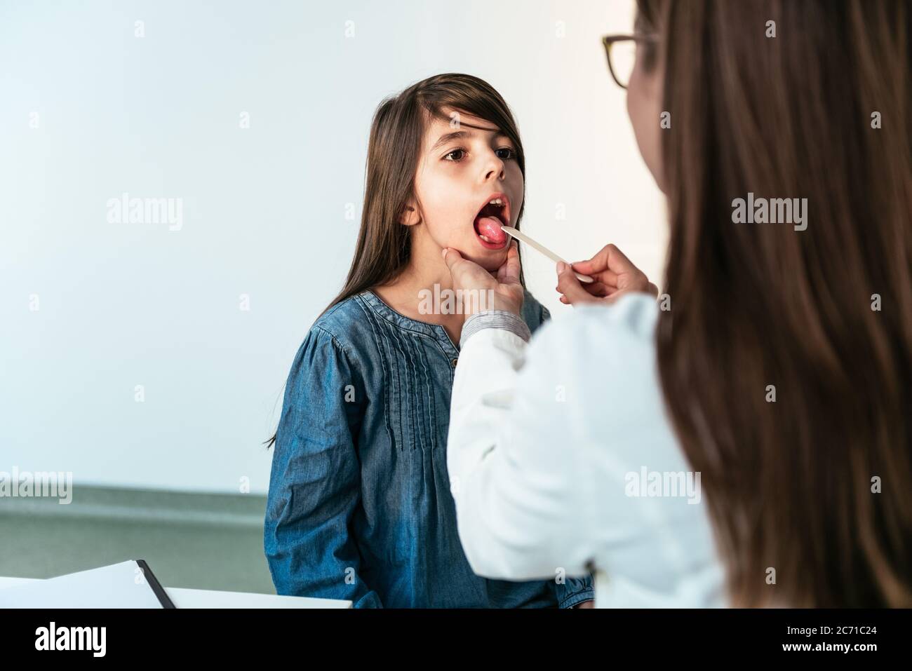 Femme médecin examinant une petite fille à l'hôpital vérifiant le mal de gorge. Le pédiatre vérifie les amygdales d'un petit patient dans la chambre d'hôpital. Banque D'Images