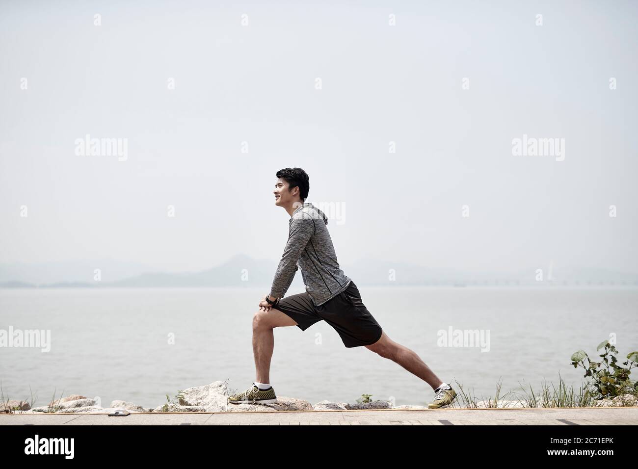 jeune homme adulte asiatique qui s'étend les jambes à l'extérieur au bord de la mer Banque D'Images