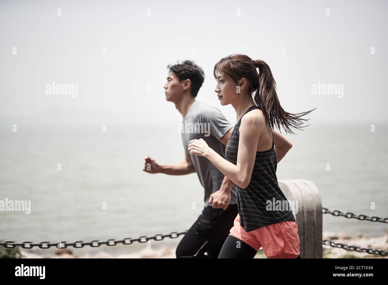 jeune asiatique homme et femme courir à l'extérieur au bord de la mer, vue latérale Banque D'Images