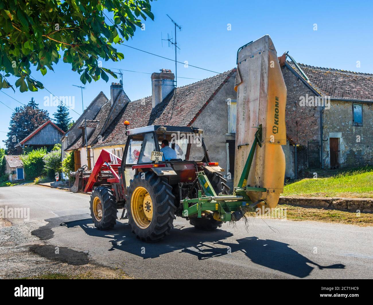 Tracteur Fiat avec foin Krone / coupe-herbe avec couvercle de sécurité traversant le village français. Banque D'Images