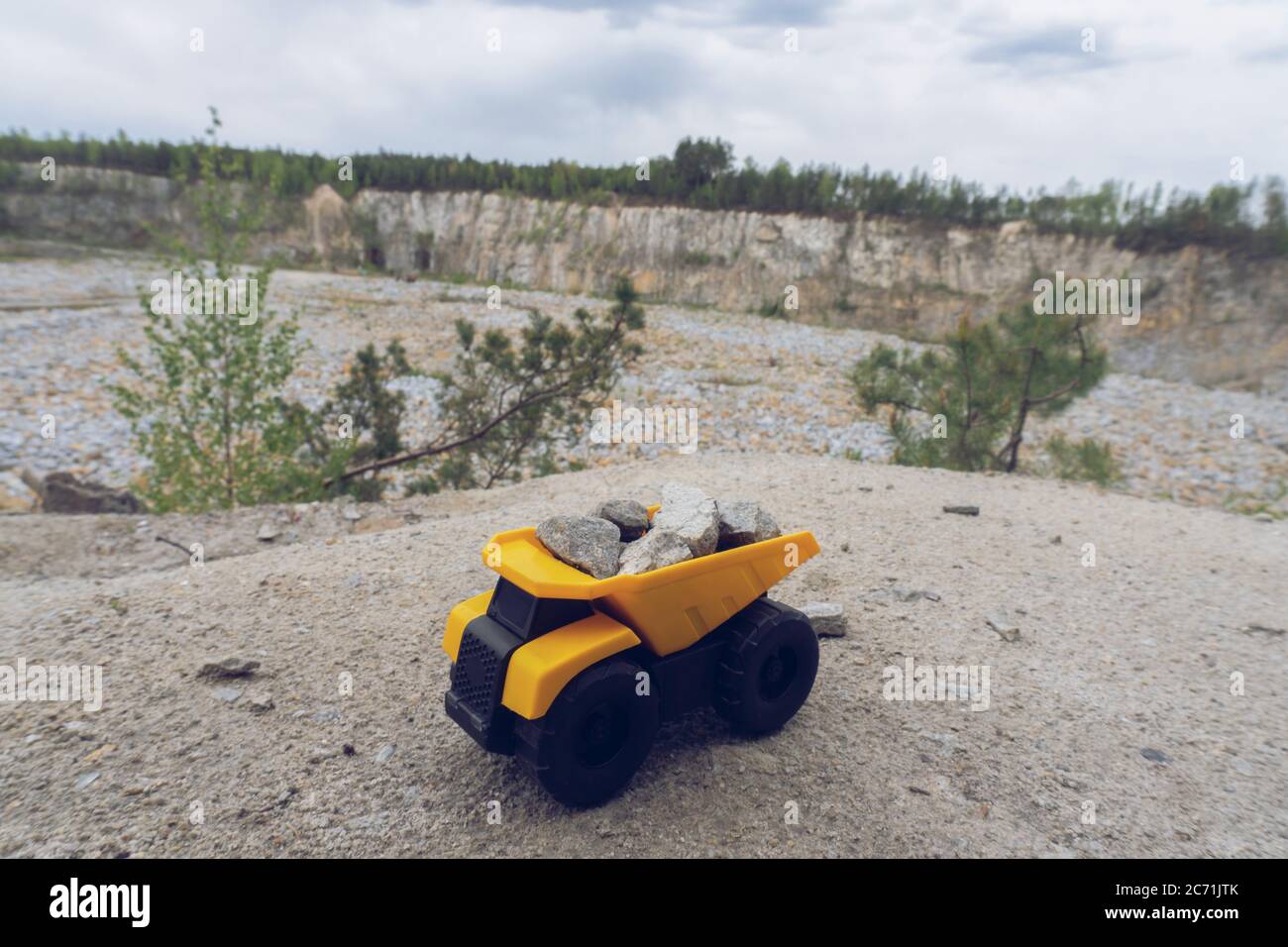 Petit jouet de voiture jaune, camion minier avec des pierres à la colline à l'arrière-plan de carrière, Banque D'Images