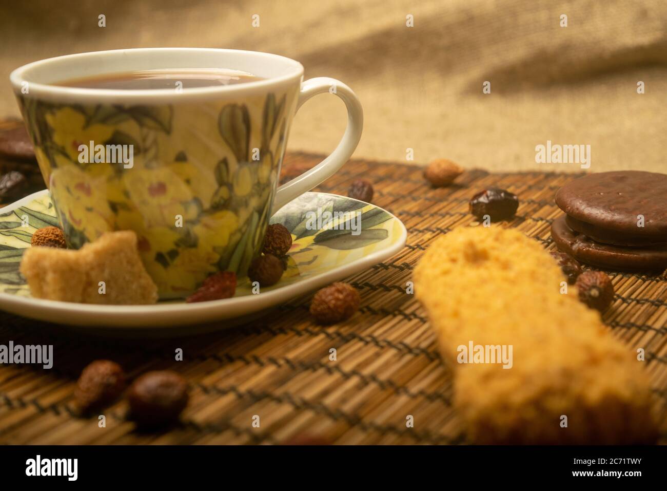 Une tasse de thé, des fruits secs de rosehip, des morceaux de sucre de canne brun et des biscuits sur un tapis de roseau. Gros plan Banque D'Images