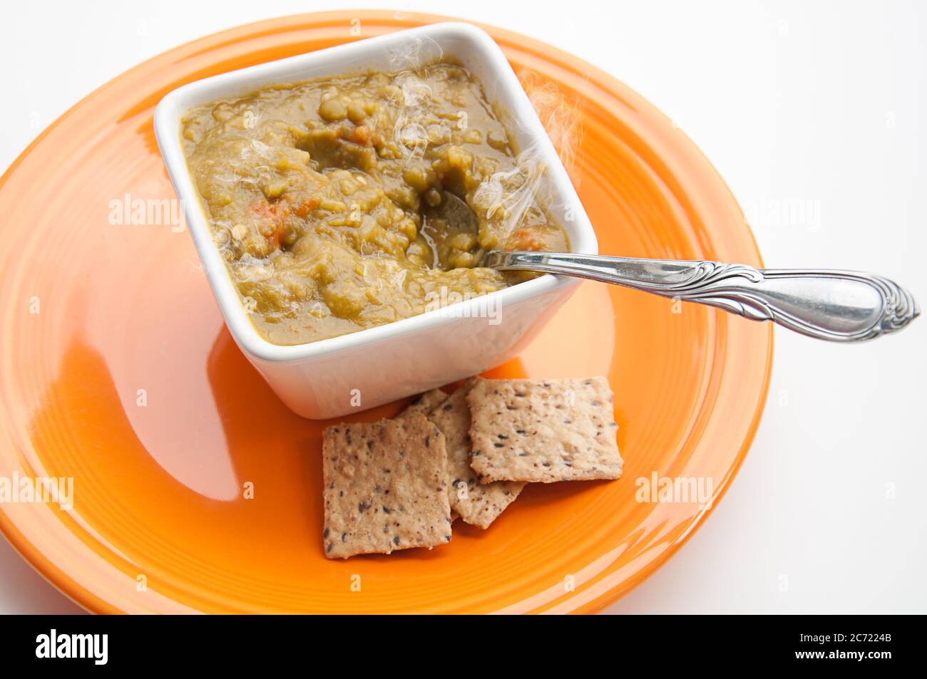 Couper la soupe aux pois et les craquelins avec une cuillère dans le bol carré blanc sur une assiette orange. Soupe chaude maison à la vapeur aliments sains pour le déjeuner ou le dîner. Banque D'Images