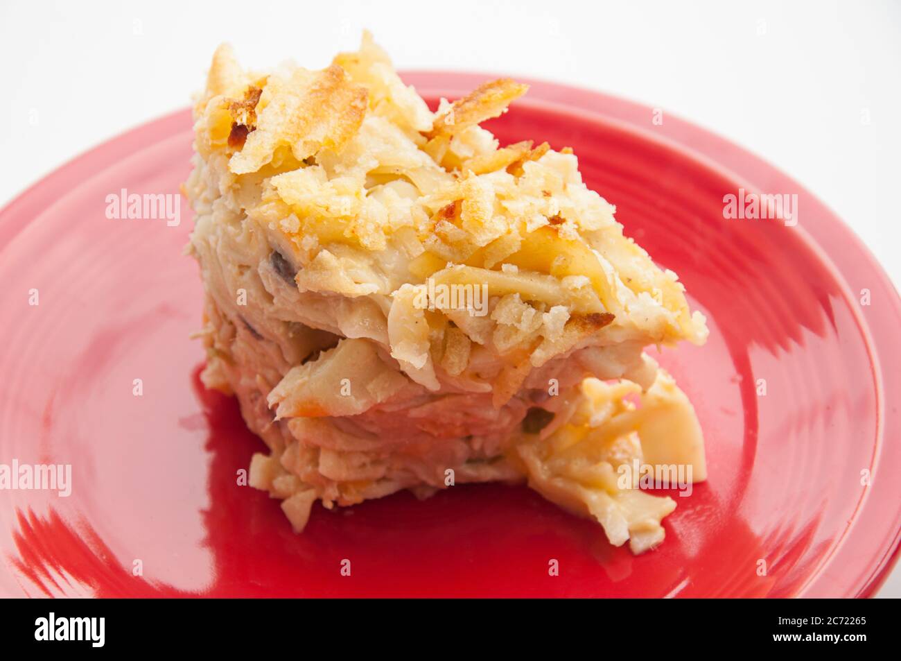 Cocotte de nouilles de thon coupée et prête à manger sur une assiette rouge. Cette casserole contient des pois et des chips de pommes de terre. Banque D'Images