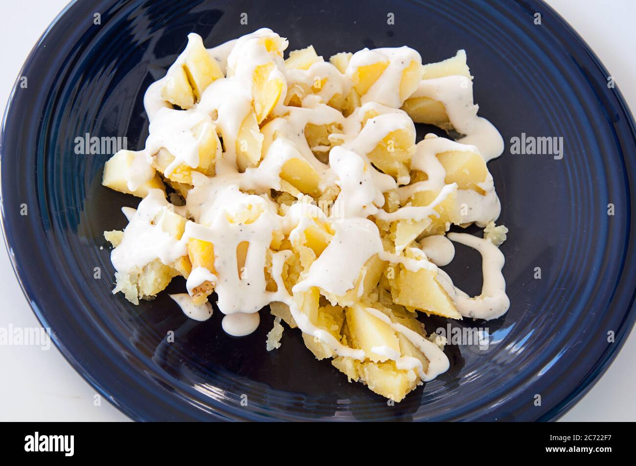 Pomme de terre cuite avec sauce ranch coupée de près sur une assiette bleu foncé. Banque D'Images