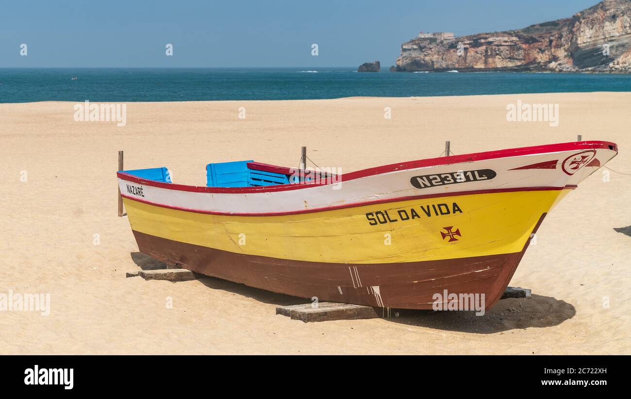 Nazaré, Portugal - avril 2018 : ancien bateau de pêche traditionnel coloré en bois sur la plage du village de pêcheurs de Nazaré.la haute falaise de Nazaré Sitio A. Banque D'Images