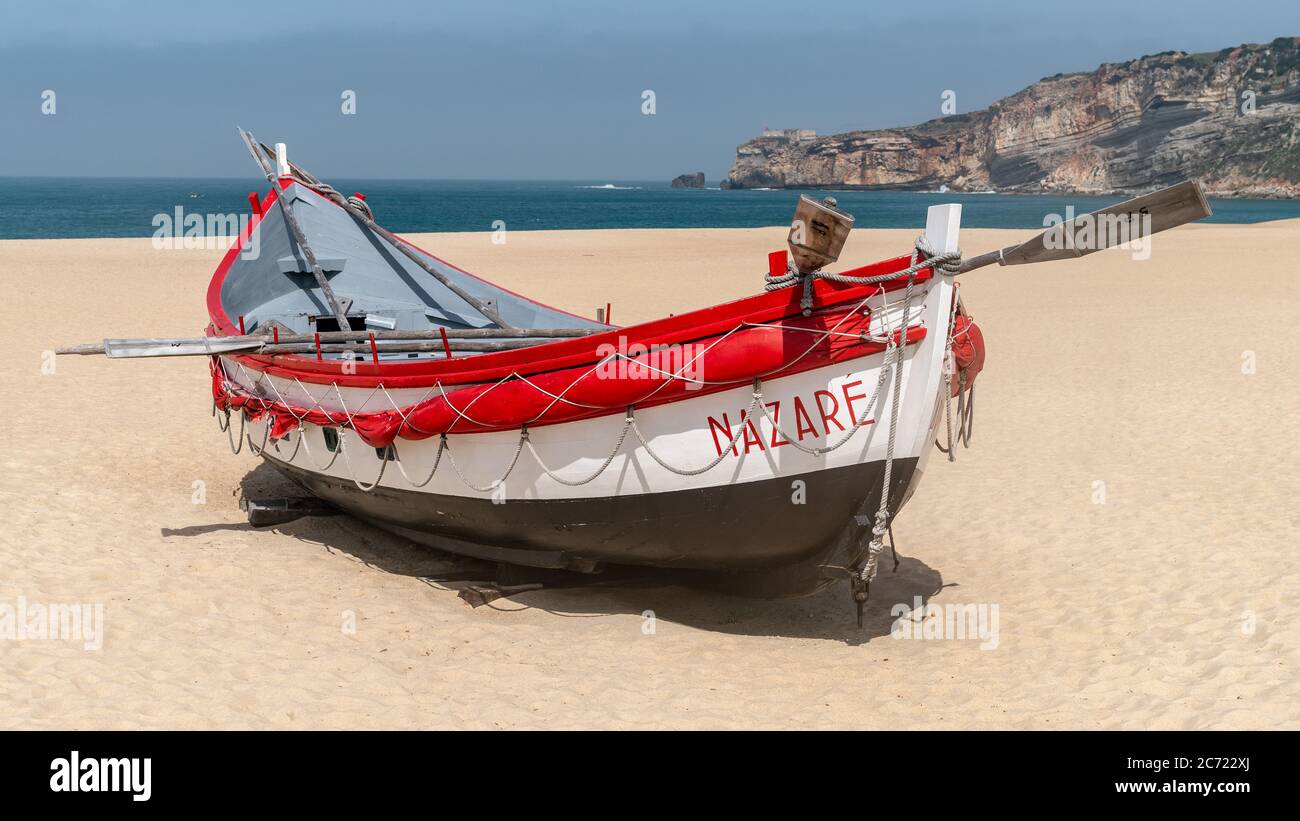 Nazaré, Portugal - avril 2018 : ancien bateau de pêche traditionnel coloré en bois sur la plage du village de pêcheurs de Nazaré.la haute falaise de Nazaré Sitio A. Banque D'Images