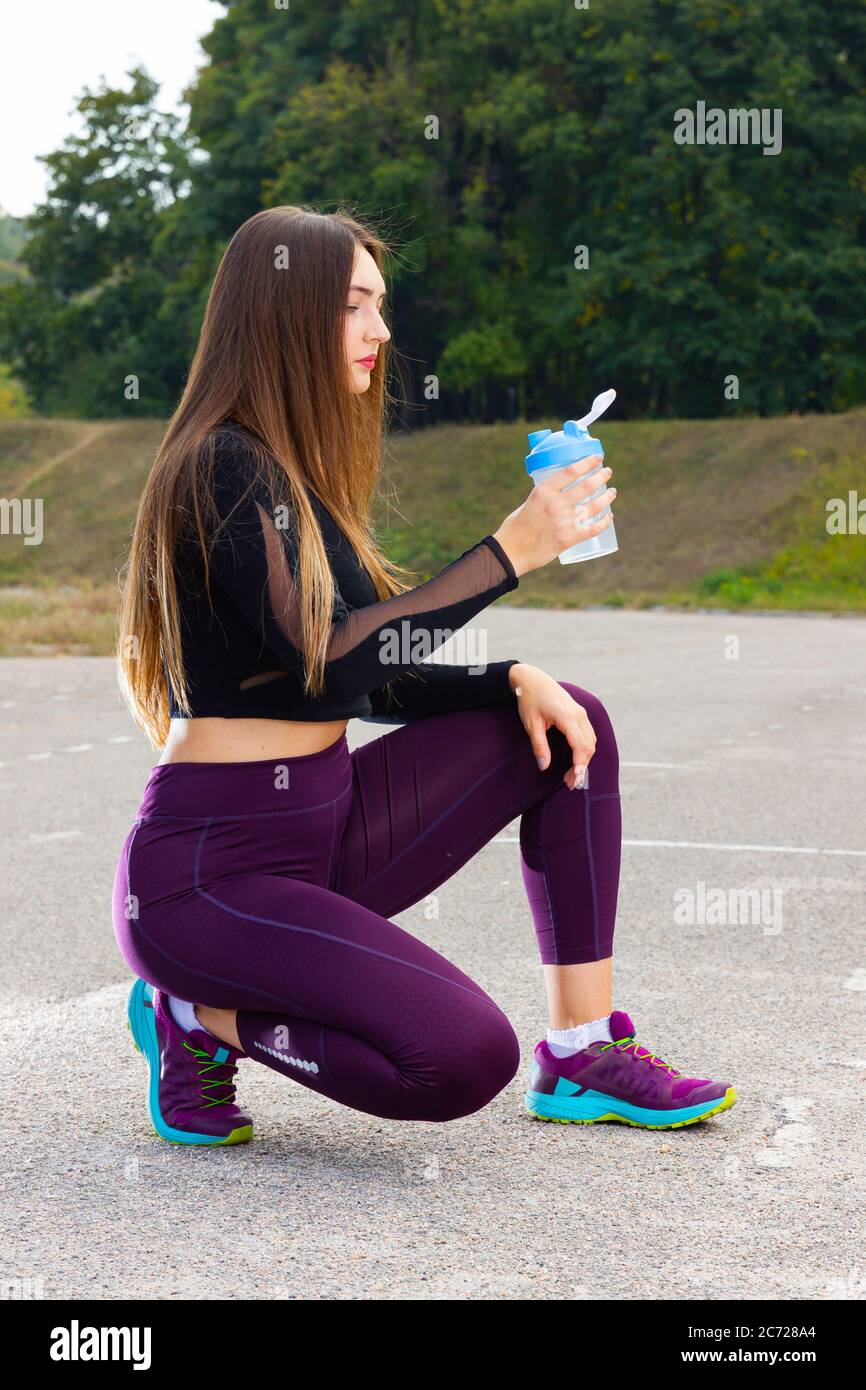 Belle jeune fille en cours d'entraînement avec eau. Une athlète féminine fait une pause pour boire de l'eau. Entraînement d'été. Fitness, personnes et vie saine Banque D'Images