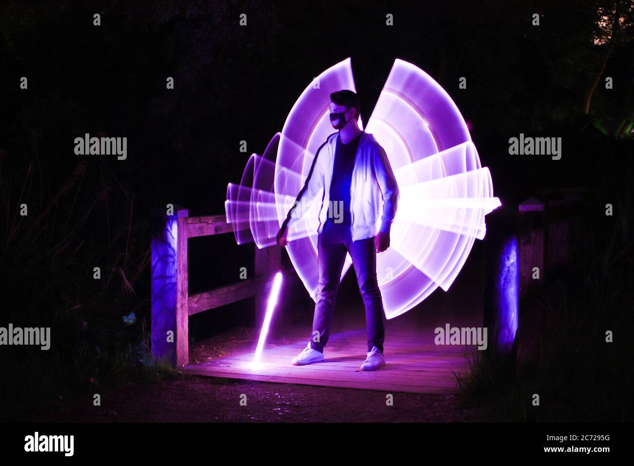 Garçon debout avec un sabre laser avec des dessins au néon et des led à la peinture lumineuse. Banque D'Images