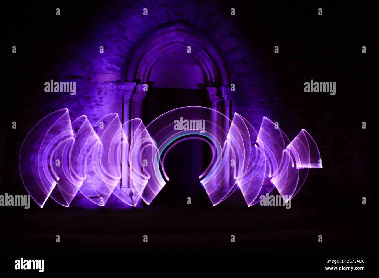 Scène de peinture lumineuse. Formes abstraites avec un sabre léger la nuit. Architecture gothique avec une arche en pierre en arrière-plan. Banque D'Images