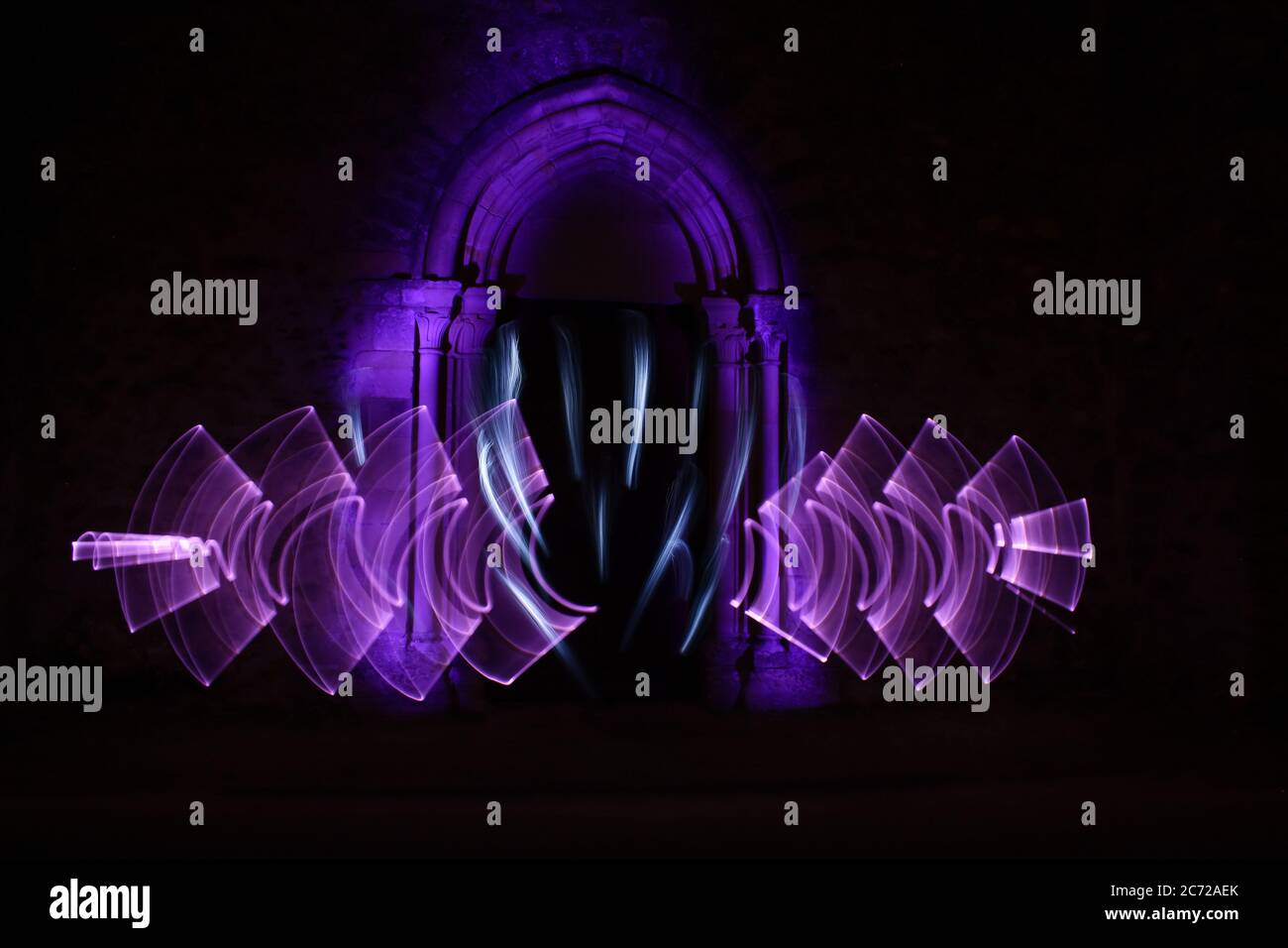 Scène de peinture lumineuse. Formes abstraites avec un sabre léger la nuit. Architecture gothique avec une arche en pierre en arrière-plan. Banque D'Images