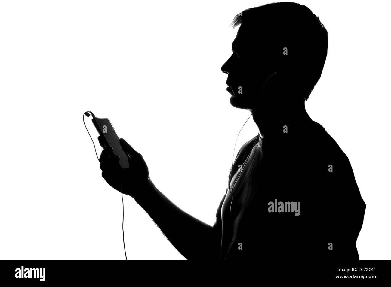 Silhouette jeune homme avec un smartphone écoutant de la musique avec un casque Banque D'Images