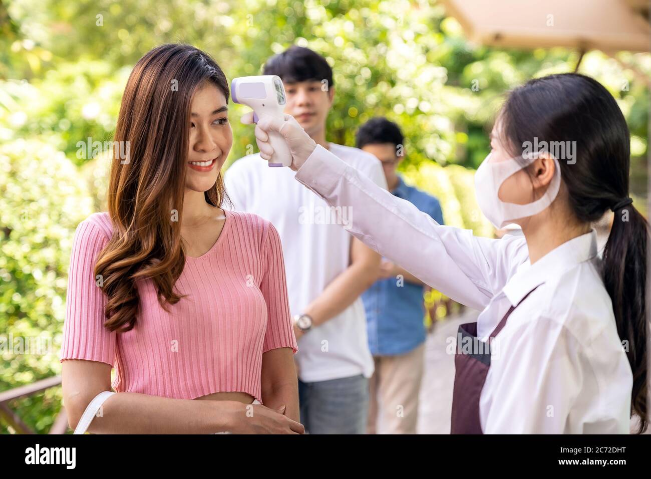 Serveuse asiatique avec masque facial Prenez le client de température avant d'entrer dans le restaurant avec la file d'attente de distance sociale dans la file. Restaurant Nouveau restaurant normal Banque D'Images