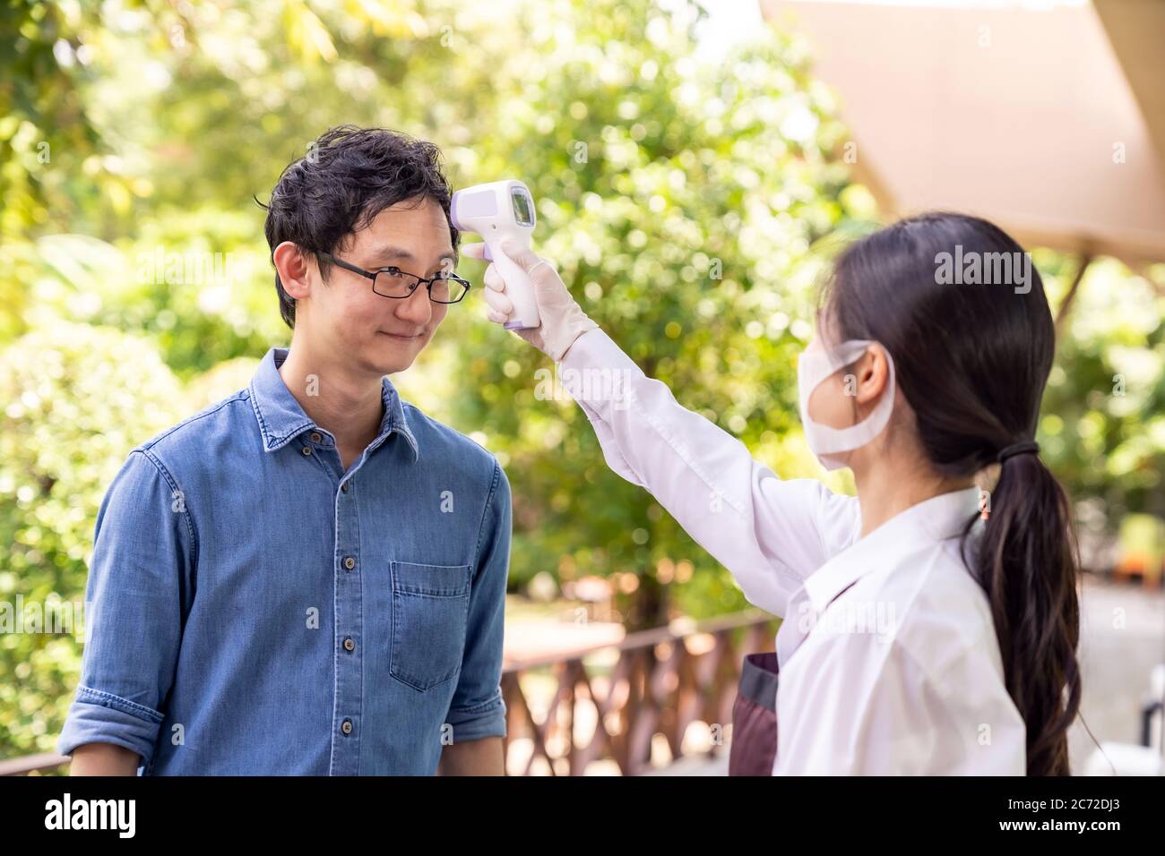 Serveuse asiatique avec masque facial Prenez le client de température avant d'entrer au restaurant. Restaurant Nouveau concept de style de vie normal de restaurant après le coronav Banque D'Images