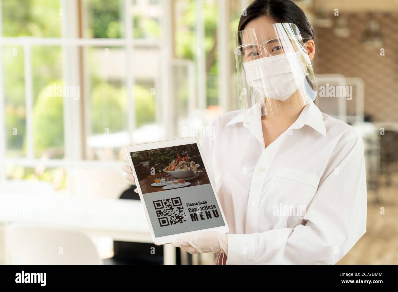 Serveuse asiatique avec masque et masque facial tient la tablette numérique avec code QR pour que le client puisse scanner le menu sans contact en ligne. Sans contact en ligne Banque D'Images