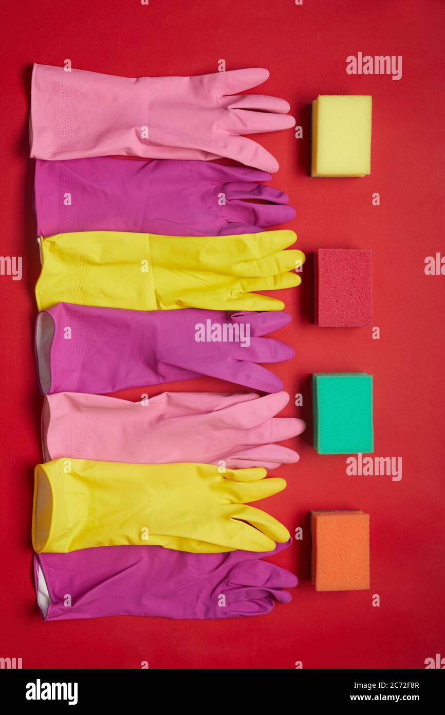 Vue à grand angle des gants en caoutchouc et des éponges couchés sur une rangée isolée sur fond rouge Banque D'Images