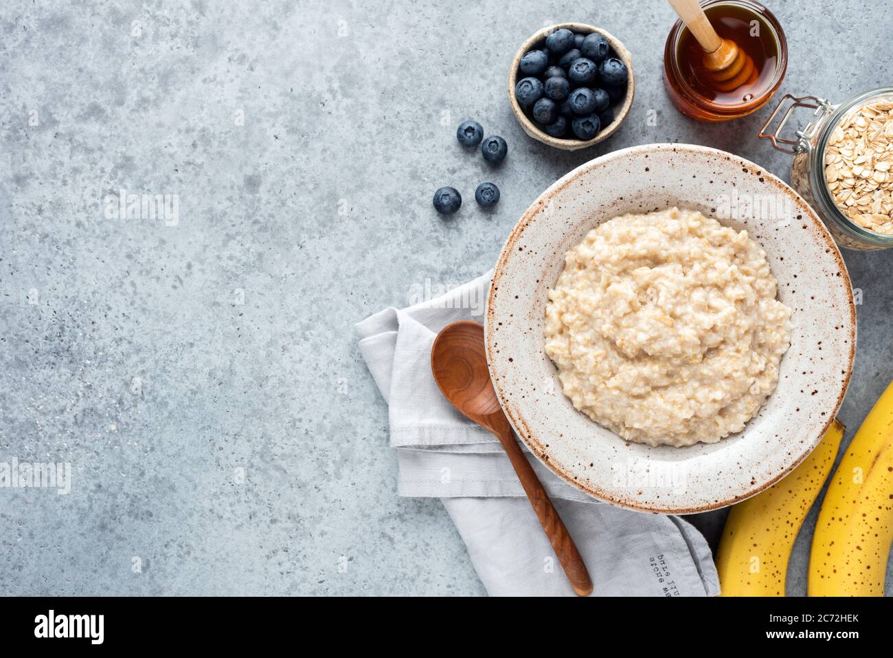 Nourriture pour le petit-déjeuner porridge de flocons d'avoine bol servi avec des fruits et du miel sur fond de béton. Vue de dessus espace de copie pour la formule ou la conception de texte Banque D'Images