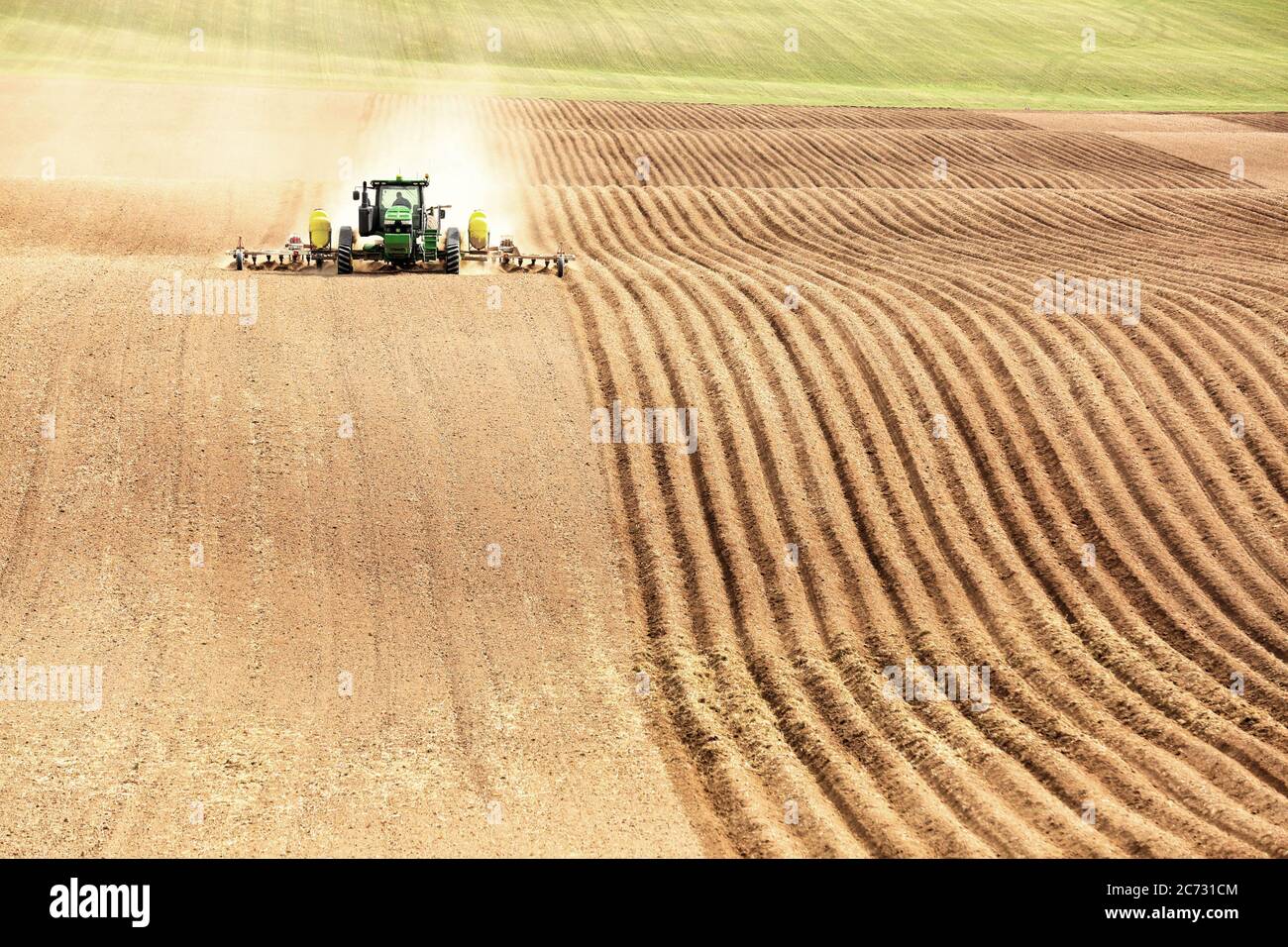 Un tracteur dans un champ de ferme, tirant un outil de labour et de culture, pour labourer et aérer le sol en préparation pour la plantation de pommes de terre de l'Idaho. Banque D'Images