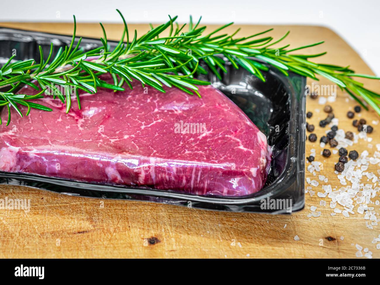 Steak de bœuf dans un emballage sous vide et épices sur planche à découper en bois Banque D'Images