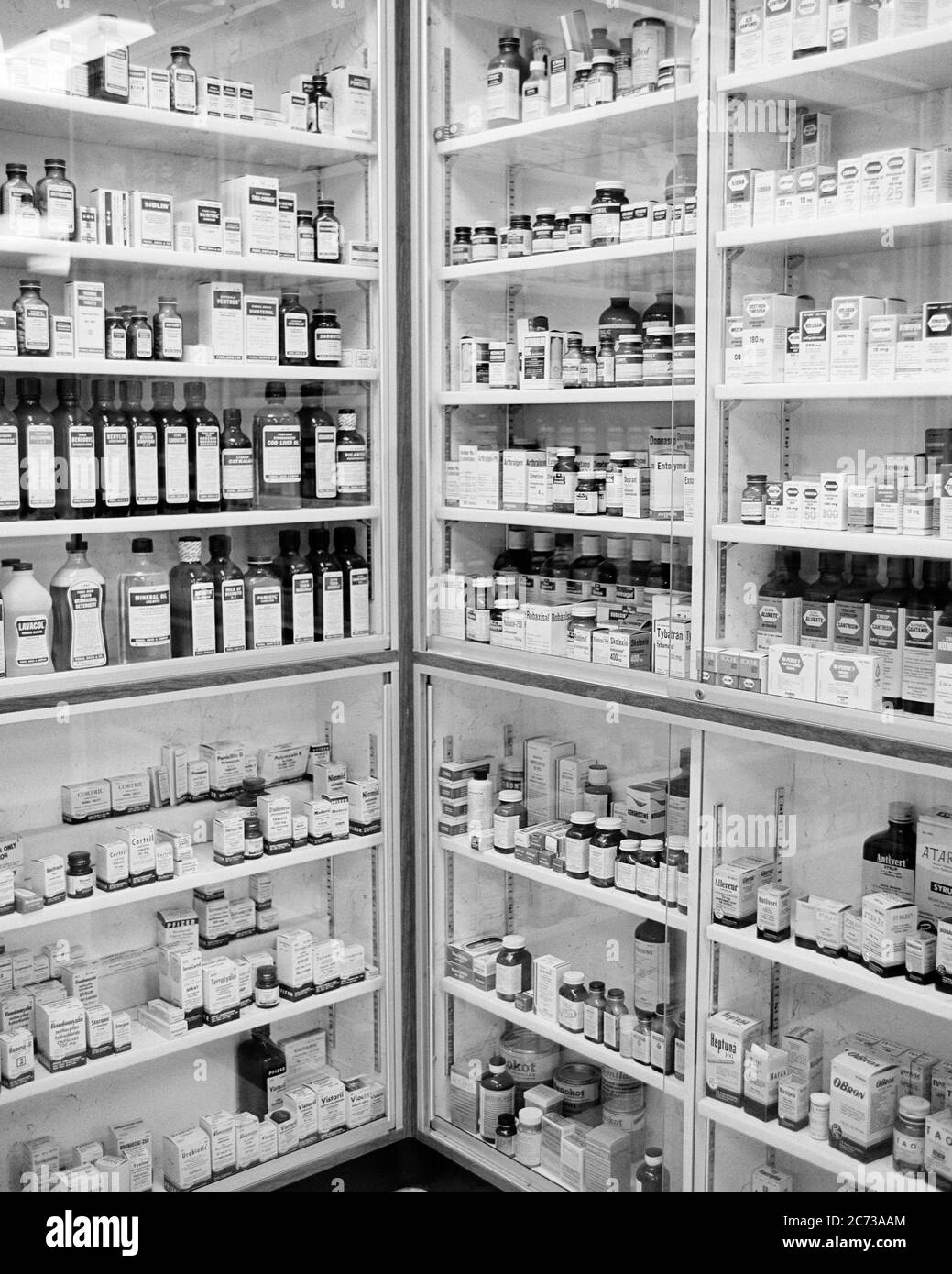 LES ÉTAGÈRES DE STOCKAGE INTÉRIEUR DE PHARMACIE DES ANNÉES 1970 CONTENANT DES FOURNITURES DE MÉDICAMENTS ET DE MÉDICAMENTS EN BOUTEILLES ET EN BOÎTES - S17402 HAR001 MÉDICAMENTS HARS PROTECTION GUÉRISON SERVICE À LA CLIENTÈLE ET DIAGNOSTIC CHOIX CONNAISSANCE PHARMACEUTIQUE PUISSANTE INNOVATION SANTÉ DANS LES MÉTIERS MAGASINS TRAITEMENT CONCEPT CONCEPTUEL REMÈDES DE VIE FIXE SYMBOLIQUE COMMERCE CONCEPTS FOURNIR NOIR ET BLANC LES ENTREPRISES MALADIE HAR001 MÉDICAMENTS ANCIENNE REPRÉSENTATION Banque D'Images