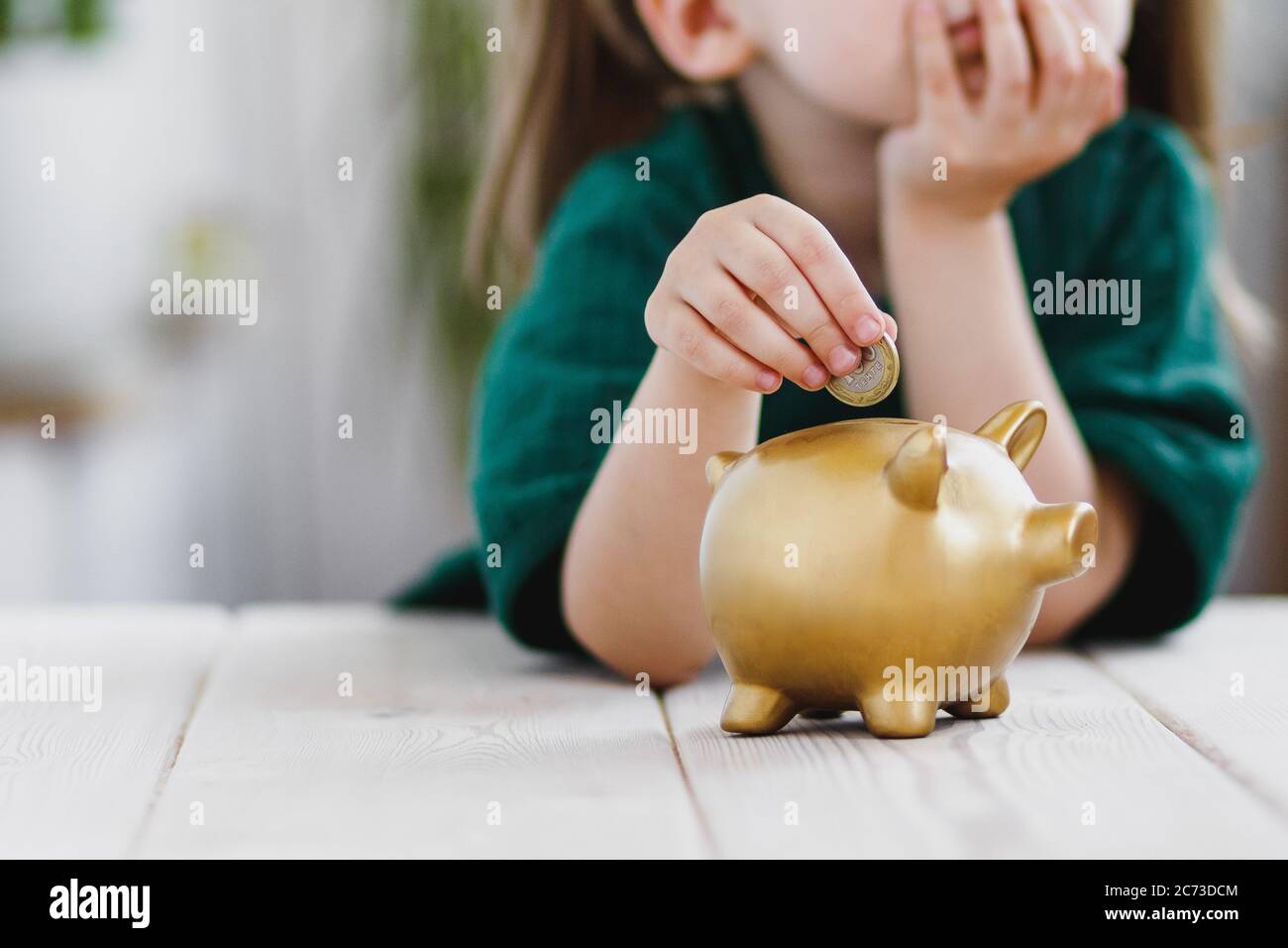 Petite fille en robe verte pensant à son argent dépenser et de mettre une pièce dans une banque de piggy. Concept d'économie d'argent Banque D'Images