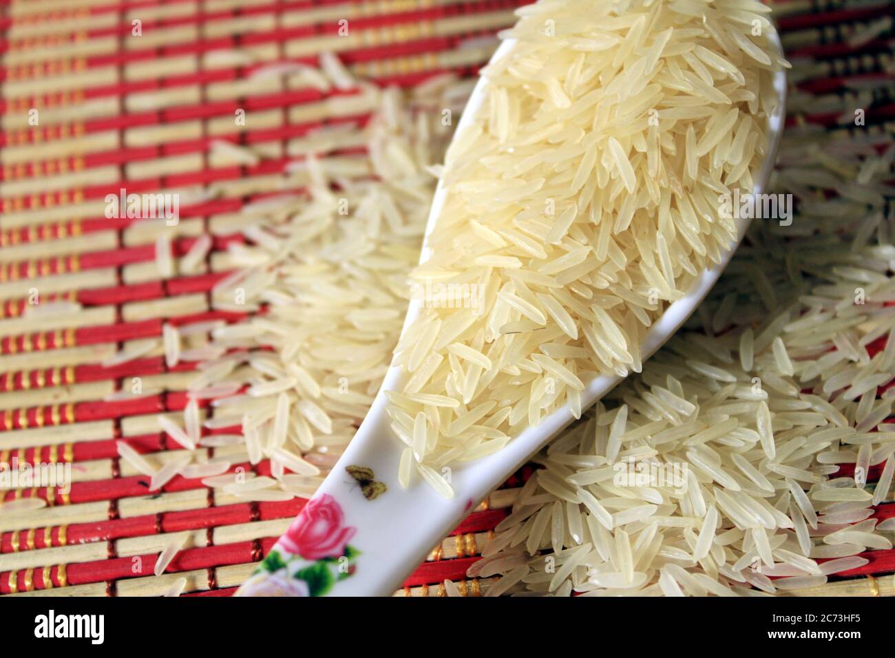 Grains de riz dans une cuillère en plastique blanc sur fond multicolore. Arrière-plan macro de riz blanc. Riz Basmati sur un tas isolé sur fond de motif. Banque D'Images