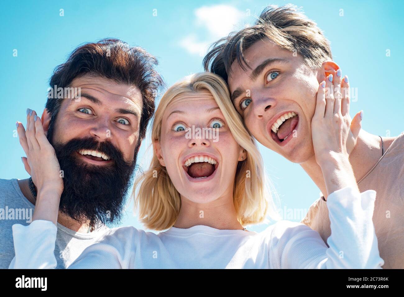 Jeunes de groupe enthousiastes - face à face. Compagnie de jeunes gens drôle à ciel ouvert. Deux garçons et une fille blonde regardant la caméra et ont Banque D'Images