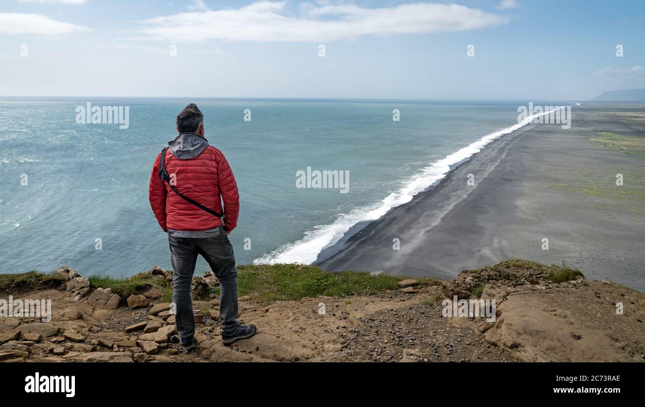 Homme non identifié surplombant l'interminable plage de sable noir volcanique située à Vik Islande Banque D'Images