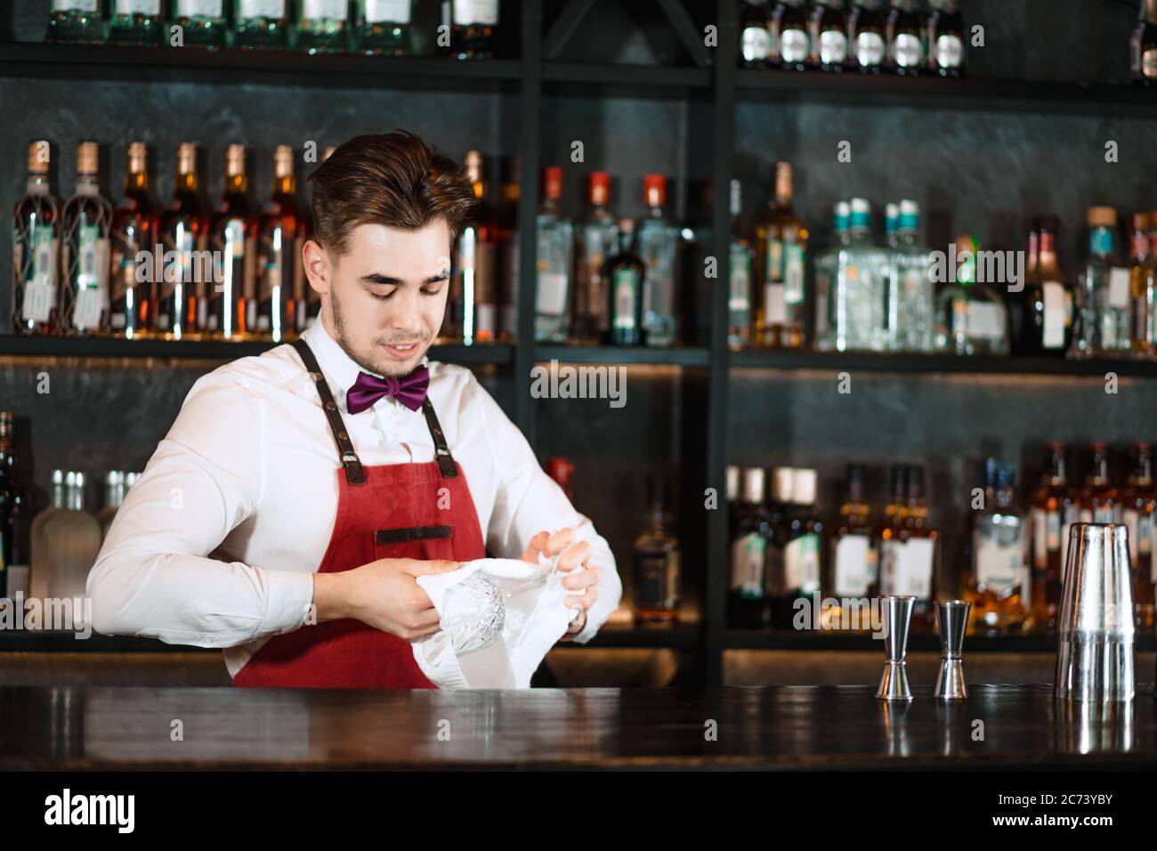 Jeune barman souriant dans le bar intérieur essuyant des verres de vigne.  Portrait de barman professionnel au travail dans la boîte de nuit nettoyage de  la tige pendant waiti Photo Stock -