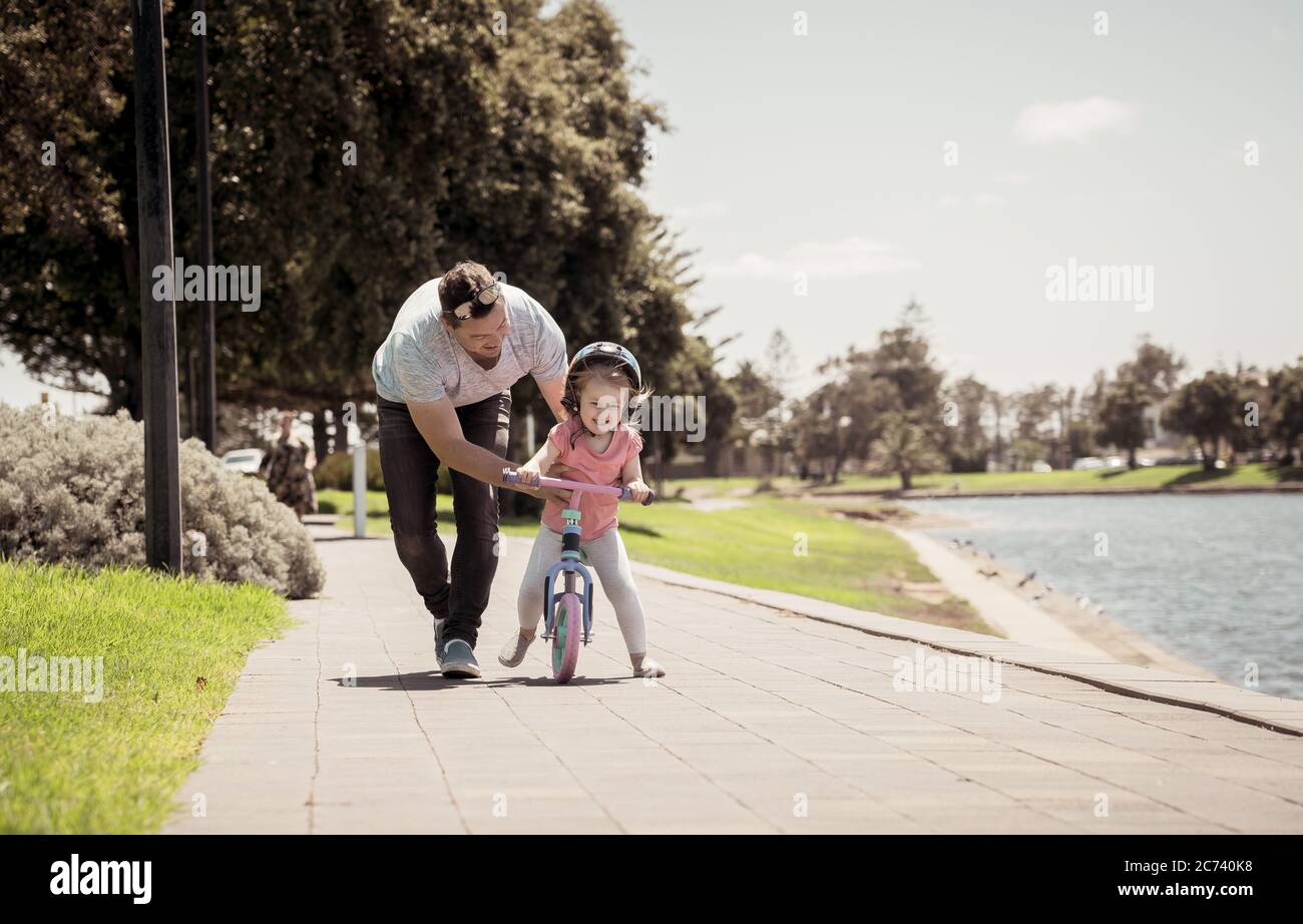 Petite fille apprenant à faire du vélo avec son père dans le parc au bord du lac. Père et fille liant et s'amuser ensemble. Bonne famille Banque D'Images