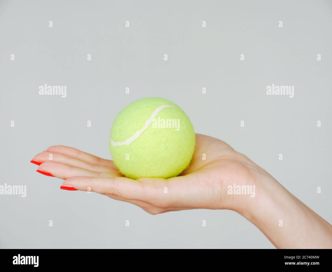 Une main féminine aux ongles manucurés rouges tient une balle de tennis verte Banque D'Images