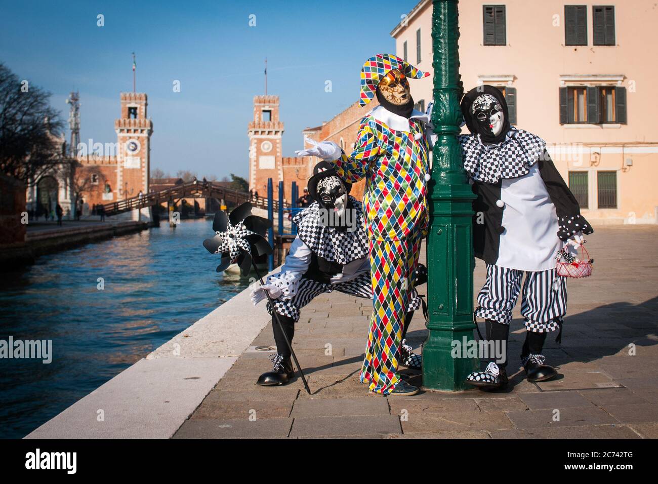 VENISE, ITALIE - 28 FÉVRIER 2020 : le masque d'Arlequin se pose avec deux autres masques noirs et blancs. En arrière-plan l'Arsenale de Venise Banque D'Images