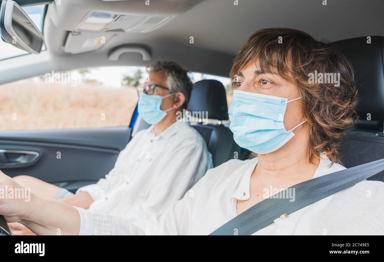Nouvelle normale. Une femme pilote avec un masque médical conduisant une voiture avec un passager. Protection de la santé. Famille dans la voiture protégé par un masque de sécurité et Banque D'Images