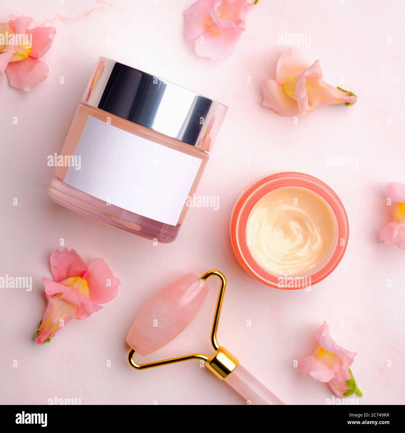 Outil de massage facial et crème cosmétique sur fond rose avec pétales de fleurs. Flat lay, vue de dessus. Soin du visage, concept anti-âge. Banque D'Images