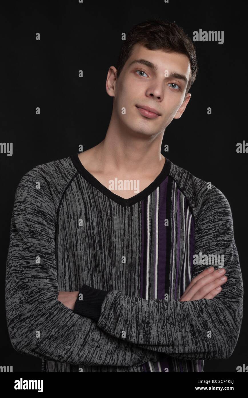 Portrait d'un jeune homme sérieux avec des mains pliées et croisant debout sur fond noir Banque D'Images