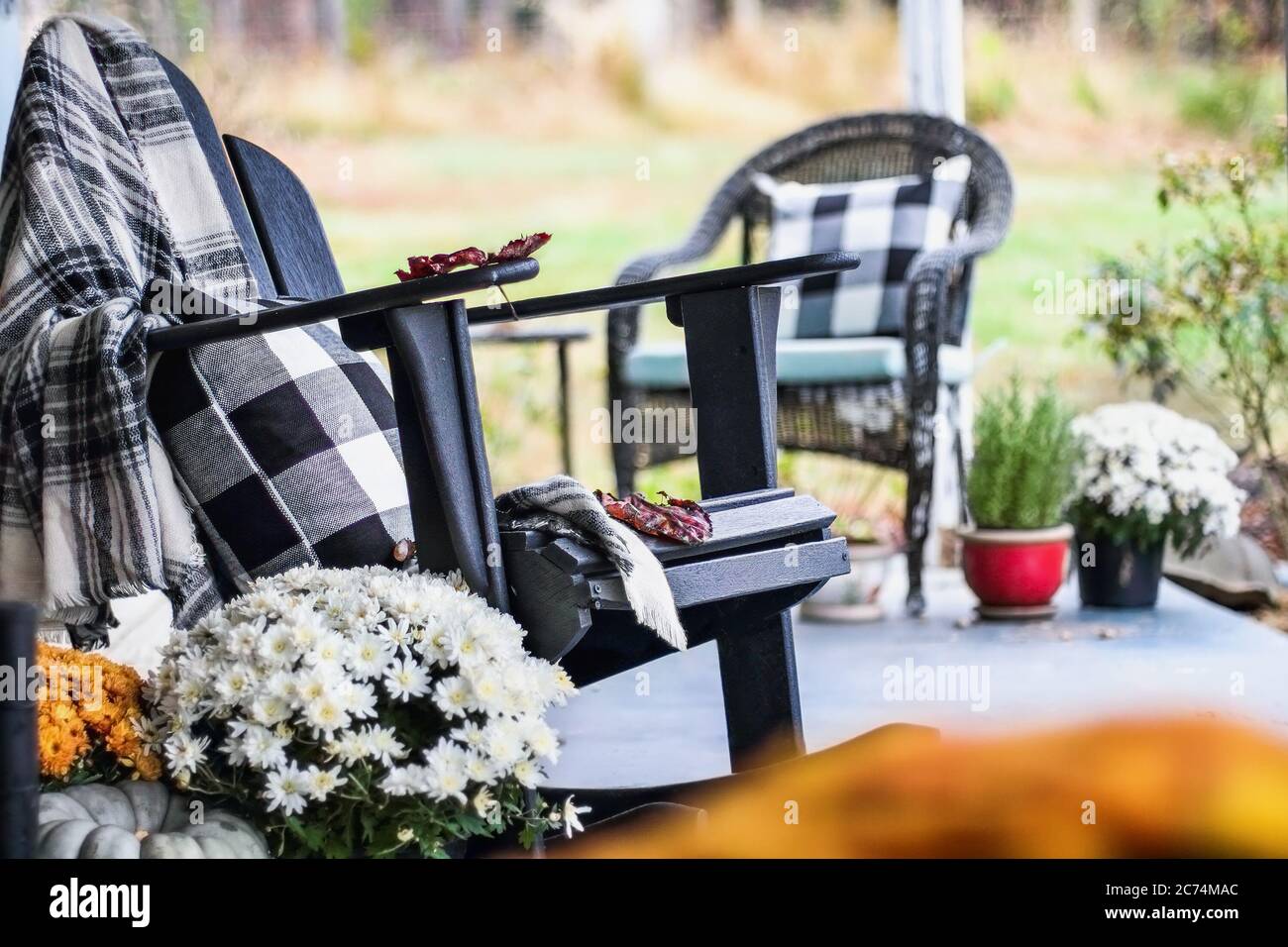 Fauteuil à bascule Adirondack avec couverture à carreaux de style traditionnel et oreillers sur une véranda ou un patio décoré pour l'automne avec des gourdes et des wh Banque D'Images