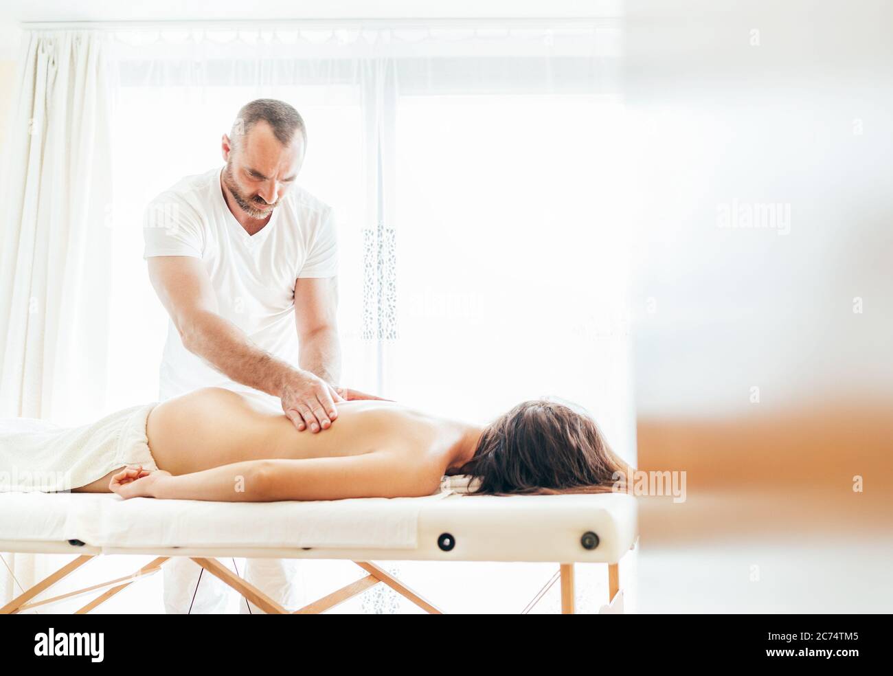 Homme de masseur barbu effectuant des manipulations de massage sur la zone lombaire pendant un massage corporel de jeunes femmes. Banque D'Images