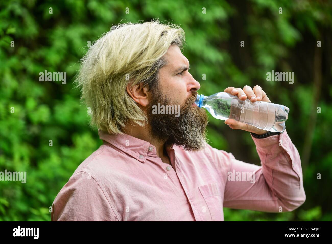 Chaleur estivale. Boire de l'eau claire. Sécurité et santé. Équilibre de l'eau. Homme barbu touriste eau potable bouteille plastique nature fond. Un gars assoiffé qui boit de l'eau en bouteille Un mode de vie sain. Banque D'Images