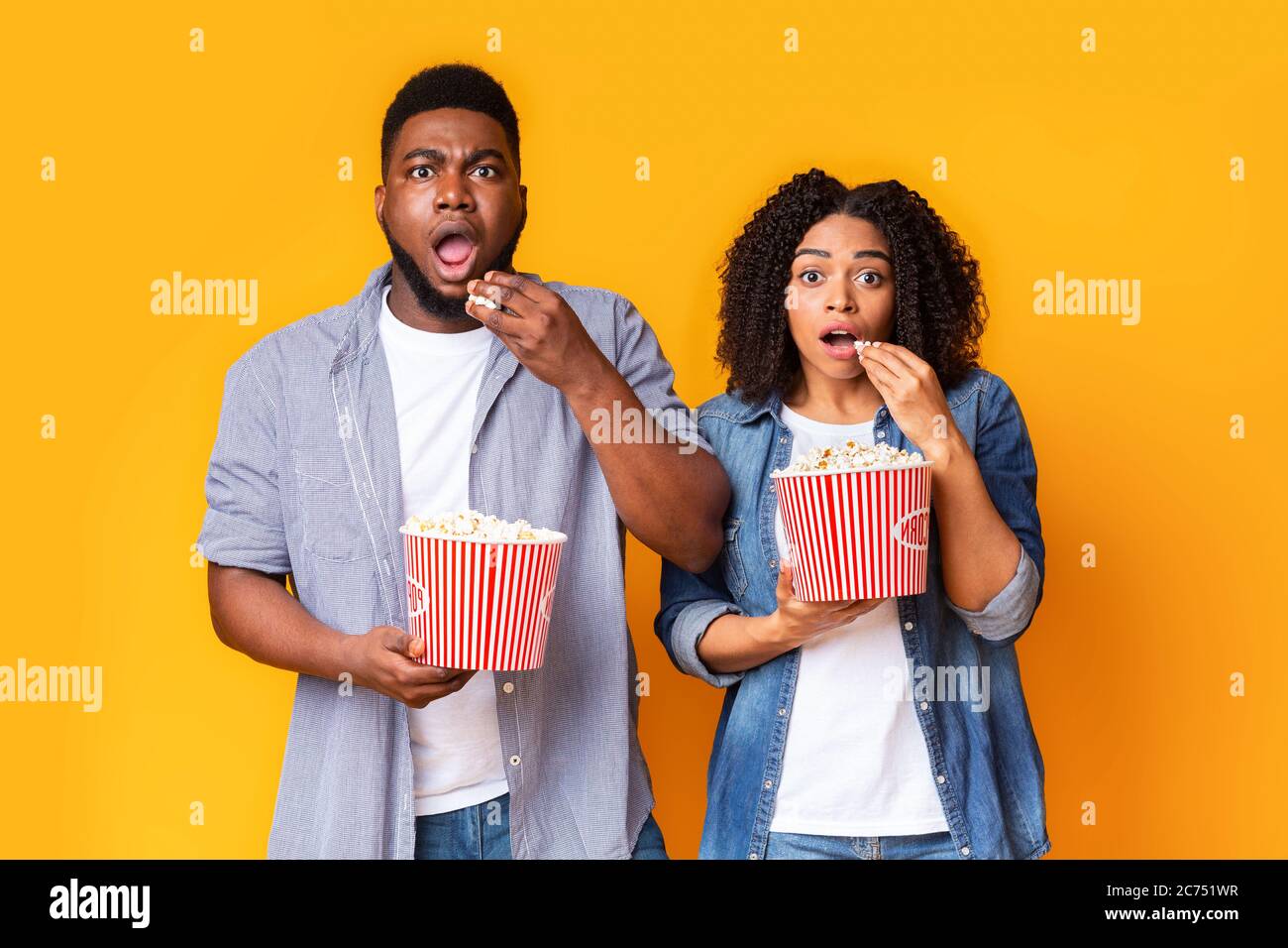 Film d'horreur. Un couple afro-américain choqué avec des seaux à maïs soufflé sur fond jaune Banque D'Images