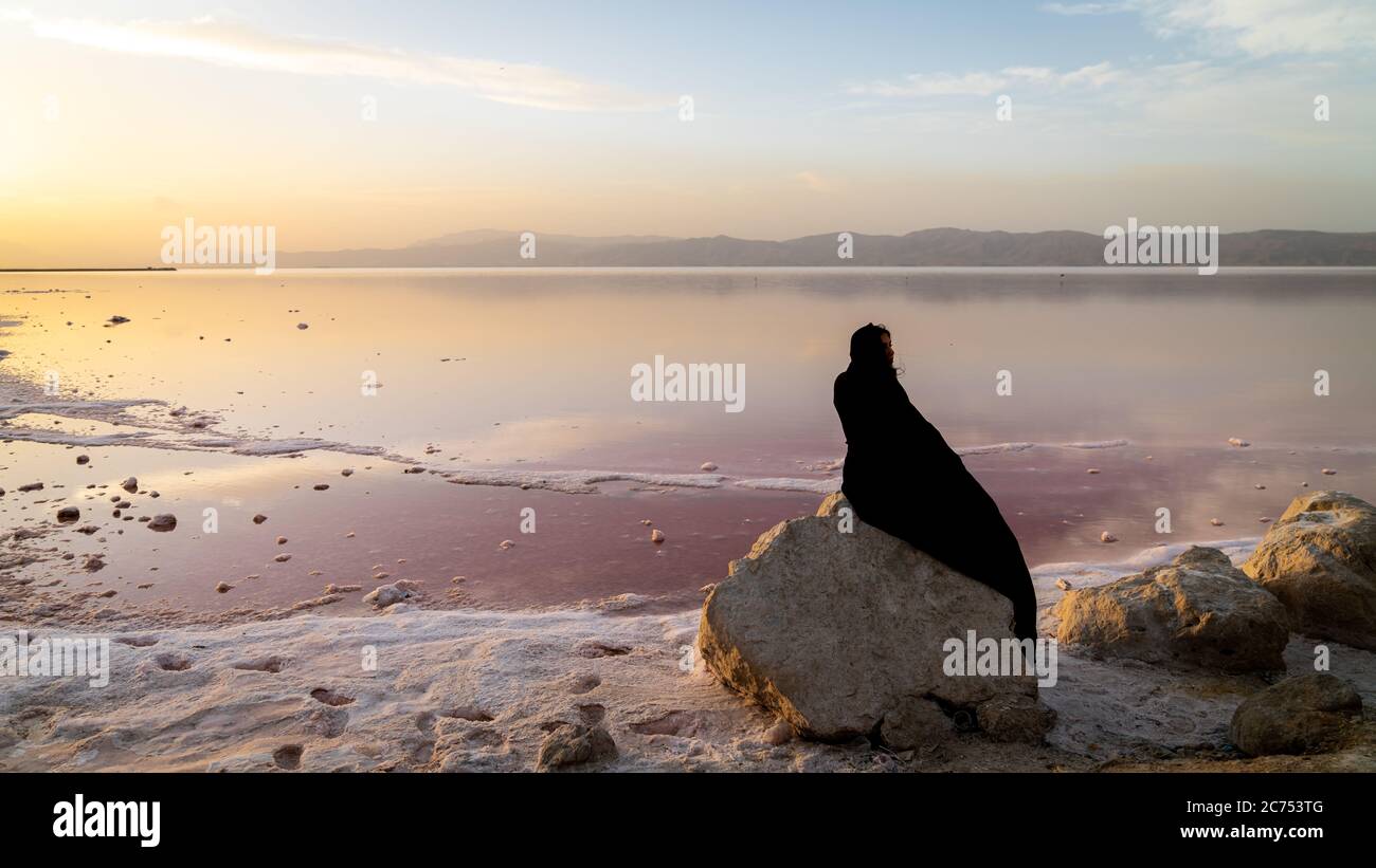 Shiraz, Iran - Mai 2019 : une iranienne non identifiée dans le burka du hijab assise sur un rocher près du lac rose du Maharaz, Iran Banque D'Images