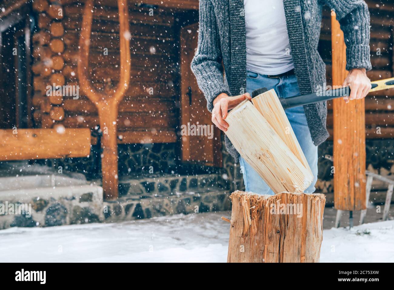 Homme hacher du bois sur cour enneigée pour une cheminée avec de lourds flocons de neige fond. Image concept vacances campagne d'hiver Banque D'Images