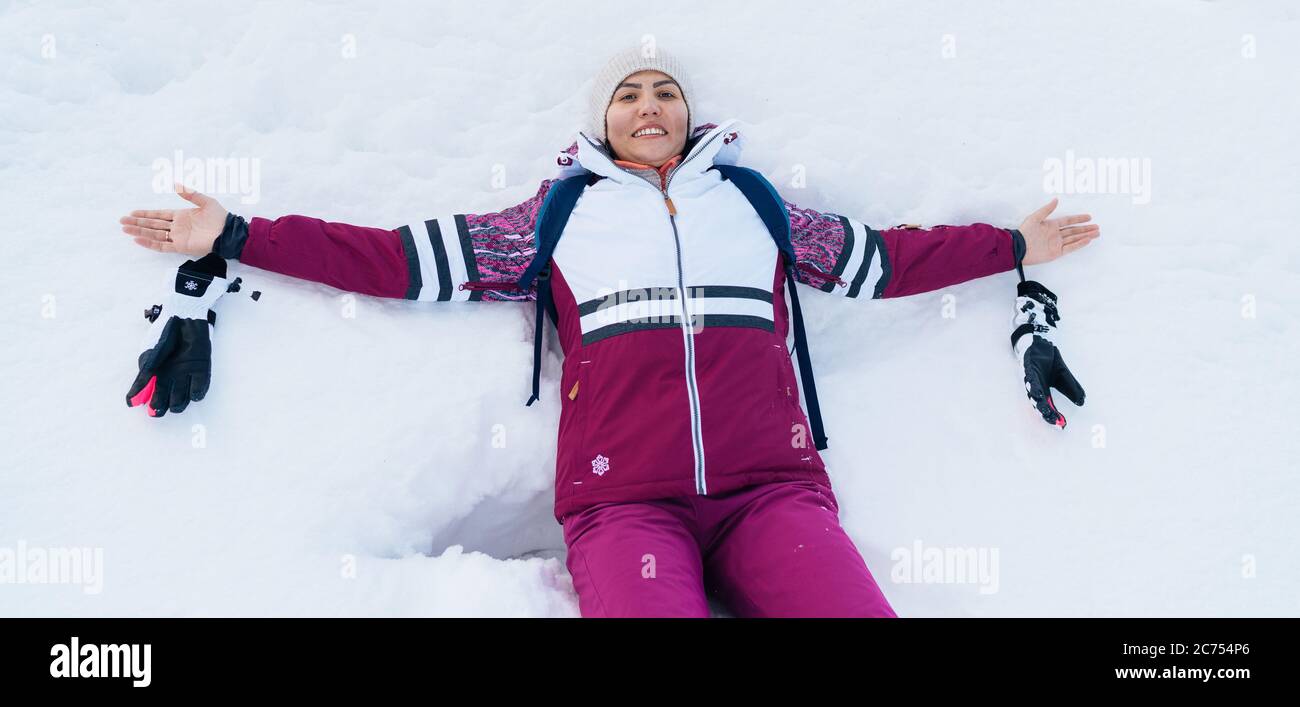Une jeune femme souriante qui se liait sur la neige blanche ouvrit les bras. Banque D'Images