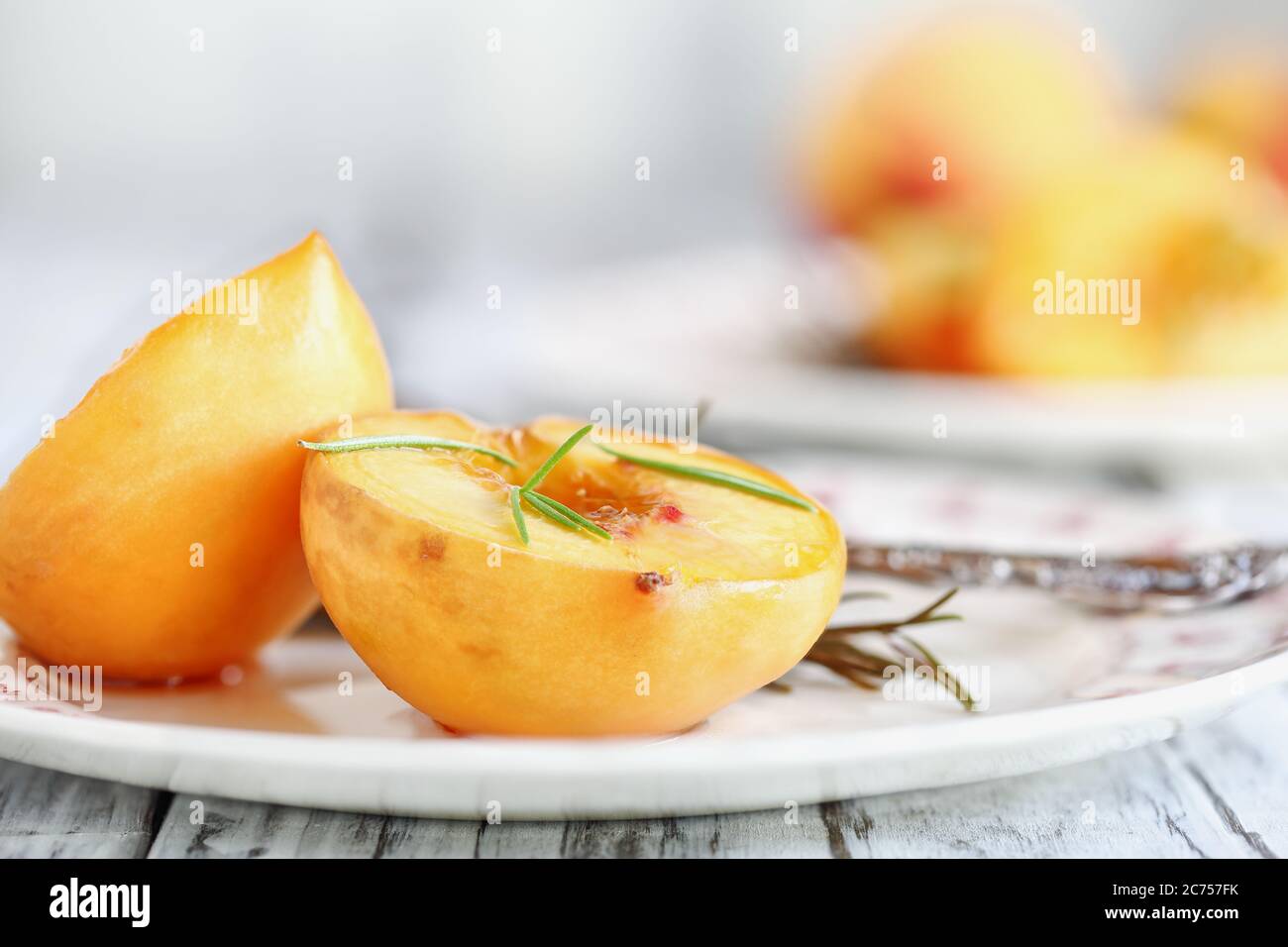 Pêches fraîches rôties maison cuites au sucre brun et branches de romarin frais. Mise au point sélective avec arrière-plan flou. Banque D'Images