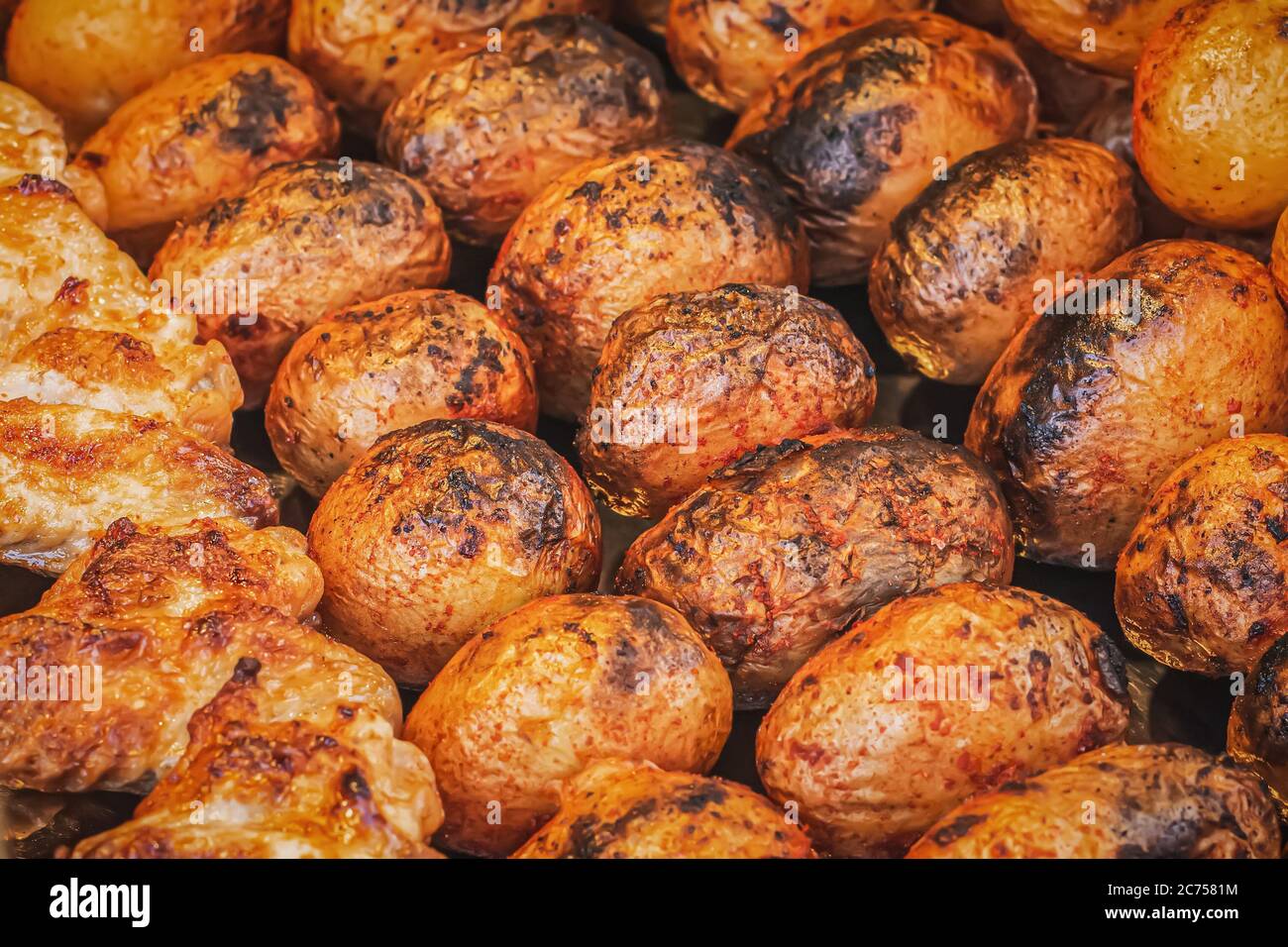 Vue latérale d'une pomme de terre cuite dans une croûte dorée. Pommes de terre frites sur brochettes sur un grill au charbon de bois dans un marché de rue. Appétissant pommes de terre savoureuses avec sp Banque D'Images