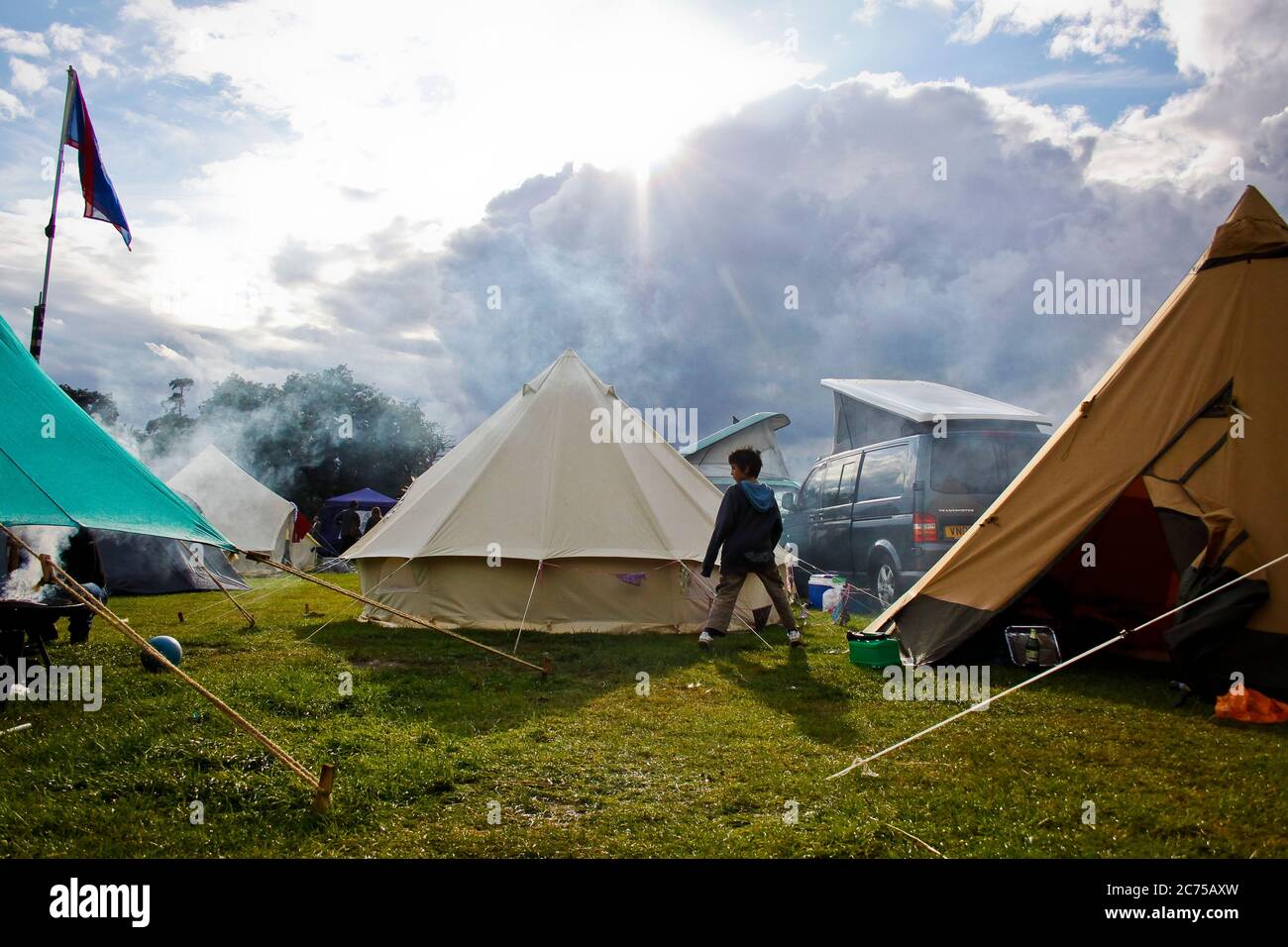 Garçon près d'une tente à cloche dans un campement de festival avec des nuages de pluie et de soleil sombres, Norfolk Banque D'Images