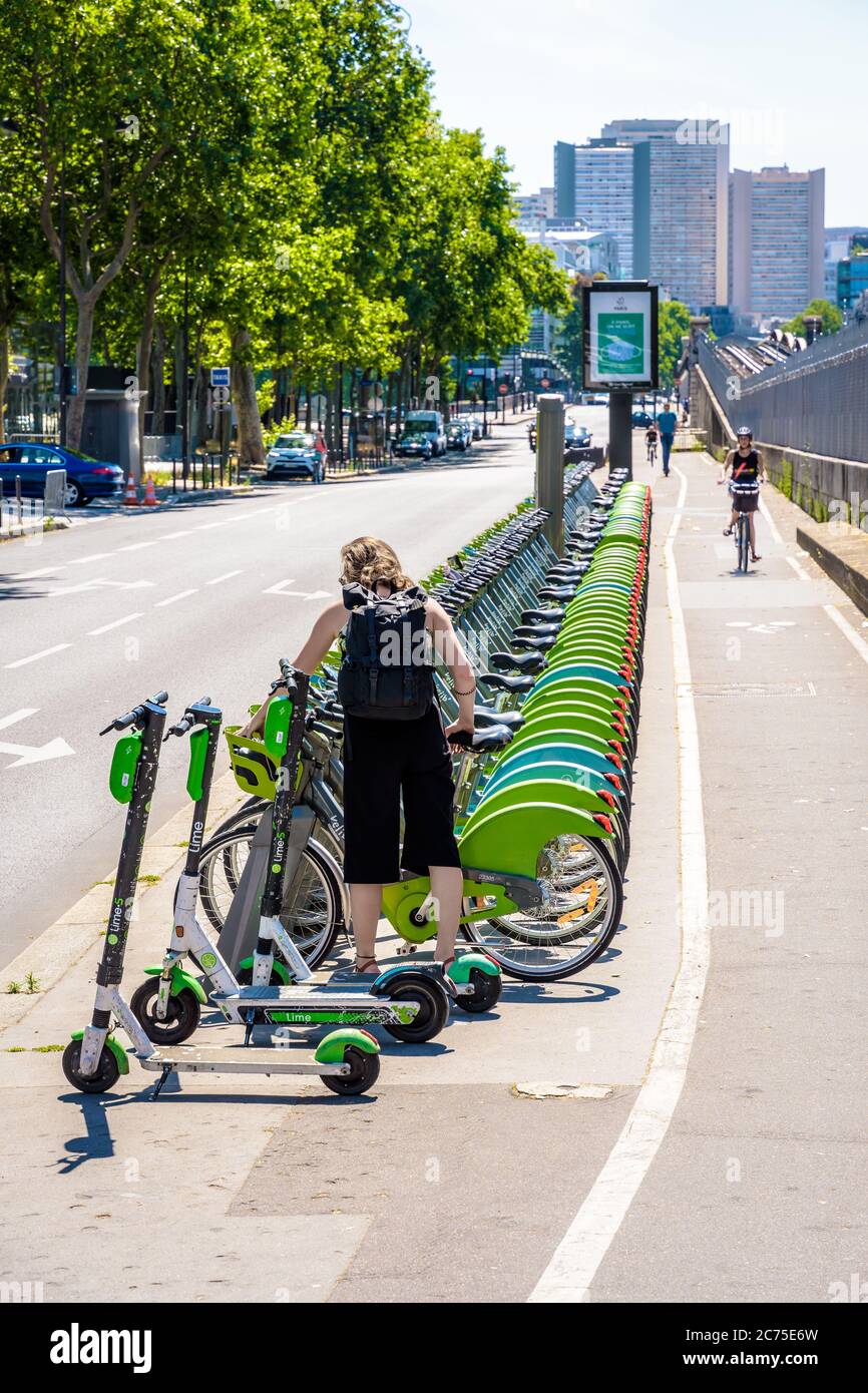 Une femme prend un vélo partagé Velib dans une rangée de vélos alignés avec soin à une station d'accueil à Paris, avec des scooters électriques Lime. Banque D'Images