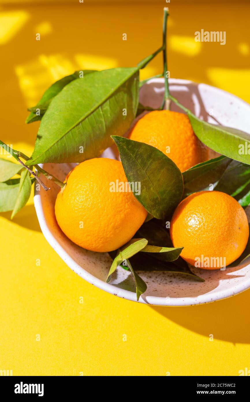 Oranges entières avec feuilles d'arbre orange sur fond jaune Banque D'Images