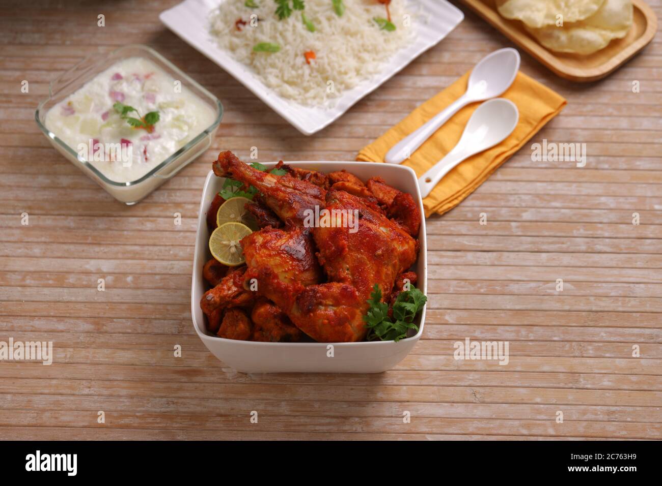 Poulet Tandoori épicé garni de feuilles de citron et de coriandre dans un bol carré blanc avec fond en bois, foyer sélectif Banque D'Images