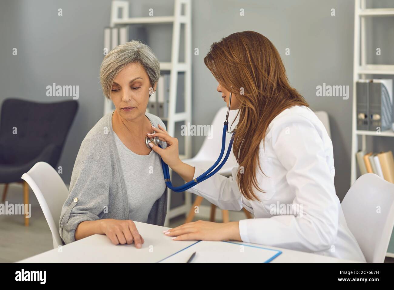 Femme âgée en visite chez un médecin à l'hôpital. Jeune travailleur médical à l'écoute du cœur du patient mature à la clinique Banque D'Images
